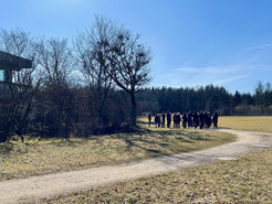 Foto mit einem Weg, Rasenflächen und kahlen Bäumen im Hintergrund und einer Gruppe von Menschen weiter hinten auf dem Weg.