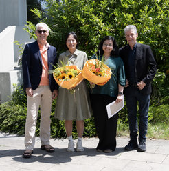 Picture with four people. Left and right two men, in the middle two women with flowers in their hands. All are smiling.